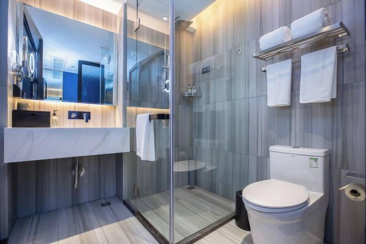 Une salle de bain moderne avec une douche à parois de verre, des toilettes blanches et un meuble-lavabo doté d’un miroir et d’un porte-serviettes.