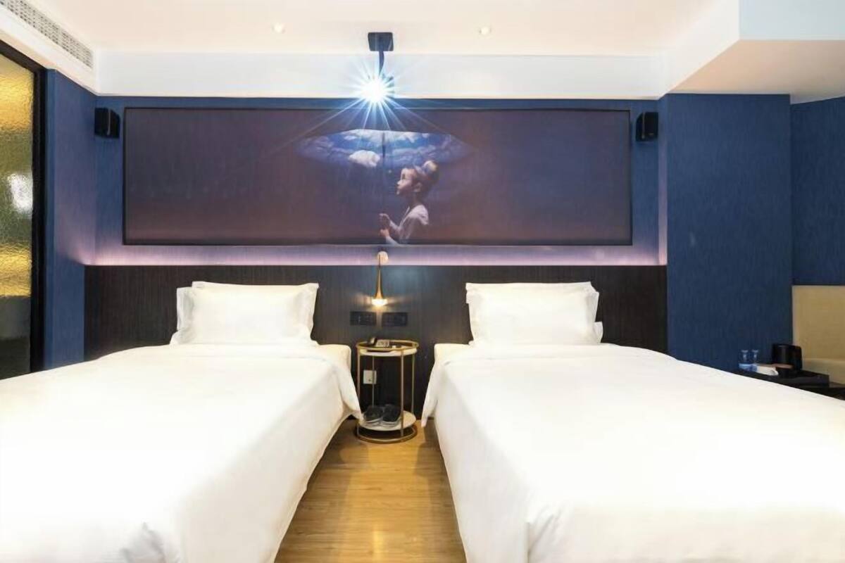 Une chambre d’hôtel avec deux lits, un grand téléviseur fixé au mur et un luminaire au plafond.