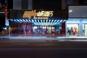 Un edificio con un letrero de neón que dice "MAX MOVIE HOTEL" y un escaparate con maniquíes mostrando ropa.