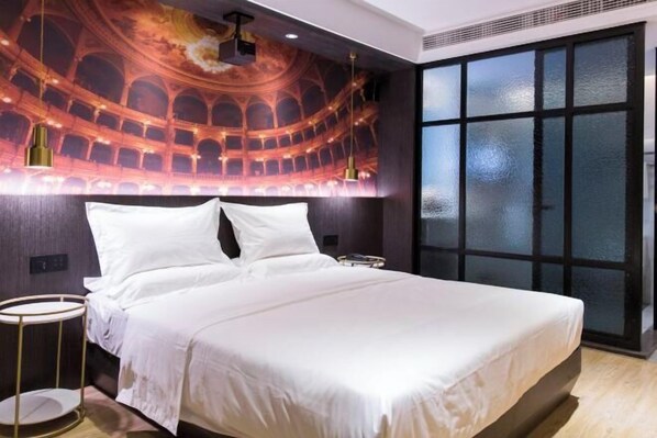 A modern hotel room with a large bed, a round side table, a ceiling mural of an amphitheater, and a large window with frosted glass.