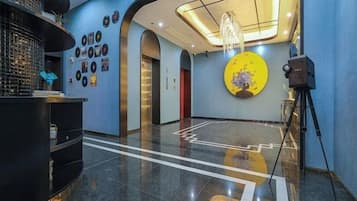 A hotel lobby with a reception desk, a large circular artwork on the wall, and a camera on a tripod.