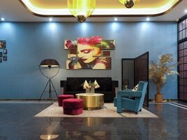 Un hall con pared azul, un cuadro grande, un sofá, una mesa de centro y una lámpara de pie.