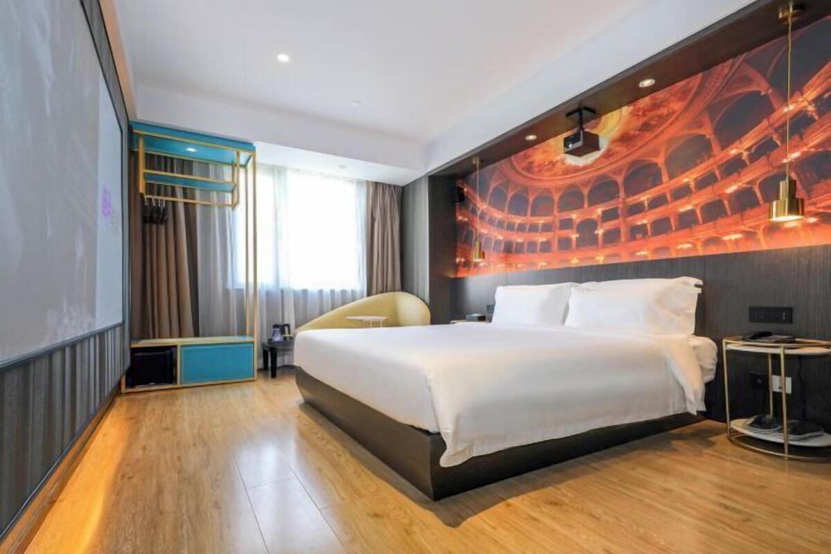 A modern hotel room with a large bed, a seating area with curtains, and a wall mural.