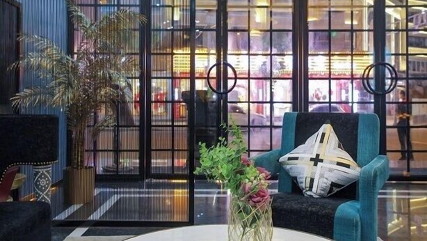 A modern lobby with a large glass window, a blue armchair, a vase with flowers, and a decorative wall panel. - Jupian Movie Hotel (Pingyang Aojiang Xinhenan Road) (Pingyang)