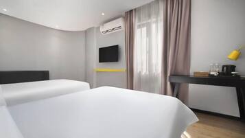 A modern hotel room with a curved ceiling, a flat-screen TV mounted on the wall, a desk with a yellow lamp, and a bed with white bedding.