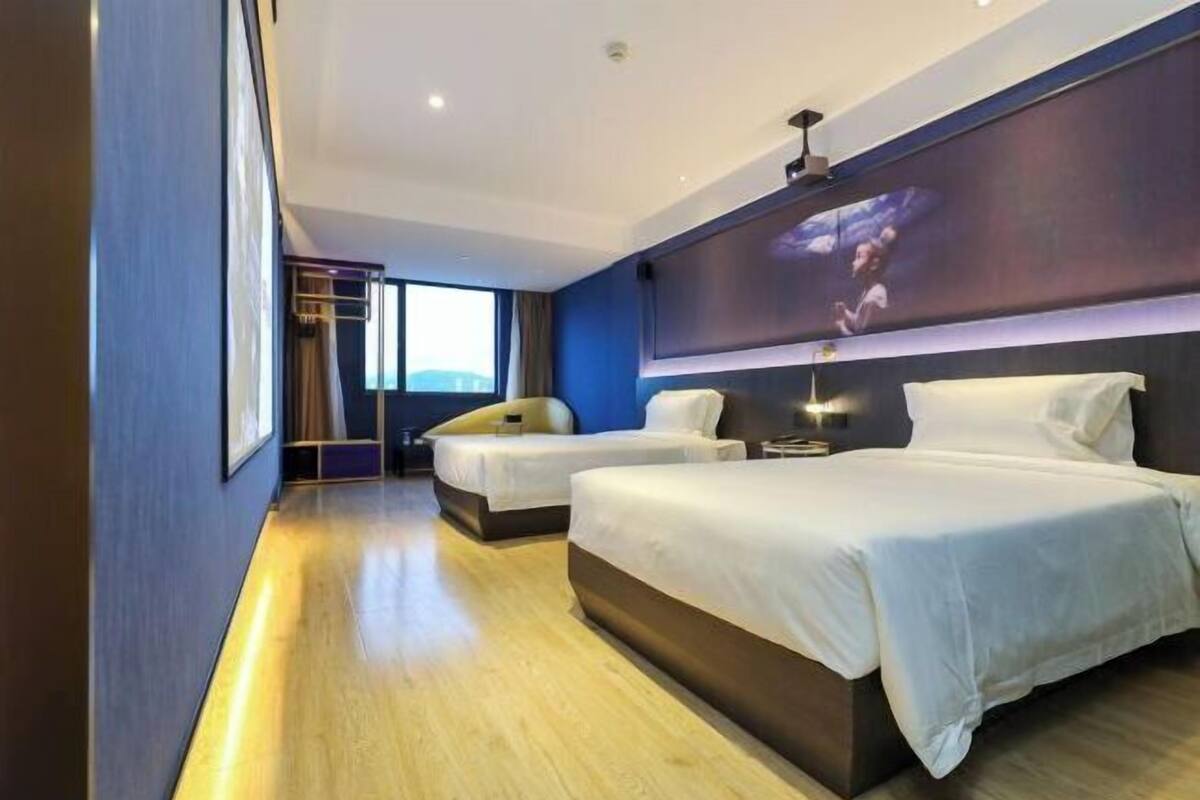 Une chambre d’hôtel moderne avec deux lits, une grande fenêtre et un téléviseur fixé au mur.