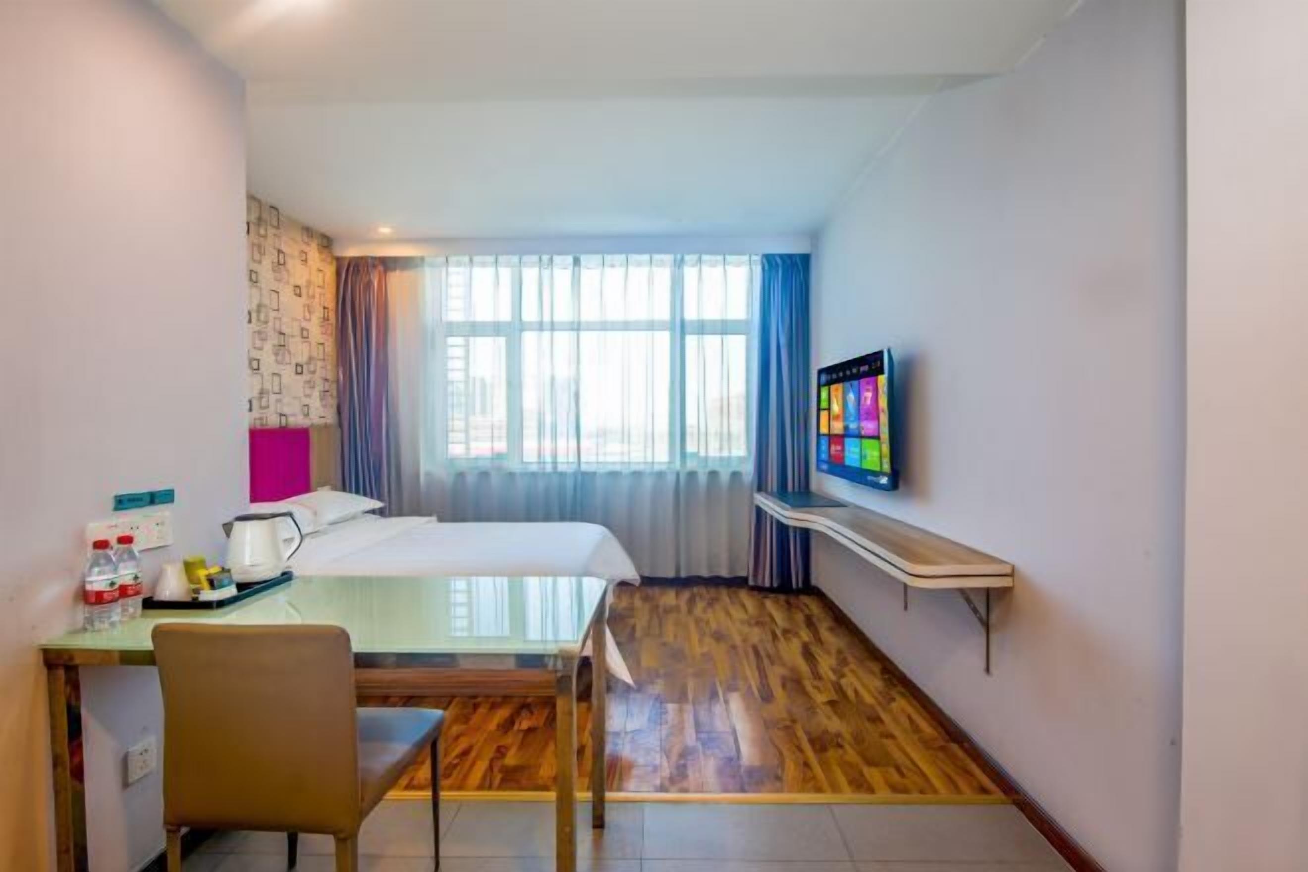 A hotel room with a bed, a desk with a chair, a television, and a window with curtains.