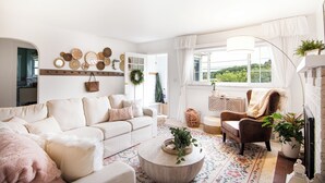 Una sala de estar acogedora con sofá, sillón y mesa de centro, decorada con obras de arte y plantas.