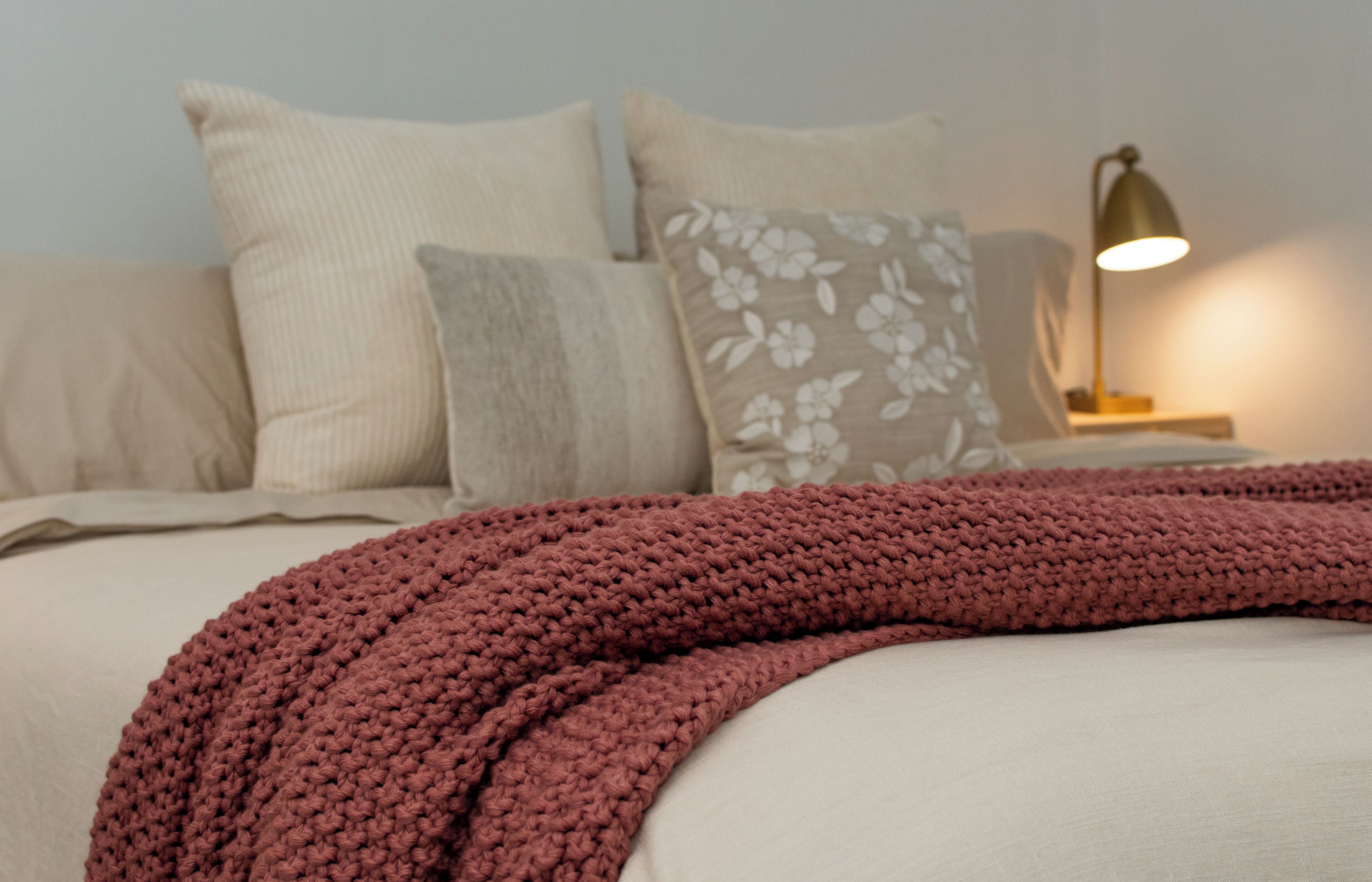 A neatly made bed with a pink knitted blanket, a beige pillow, and a floral pillow.