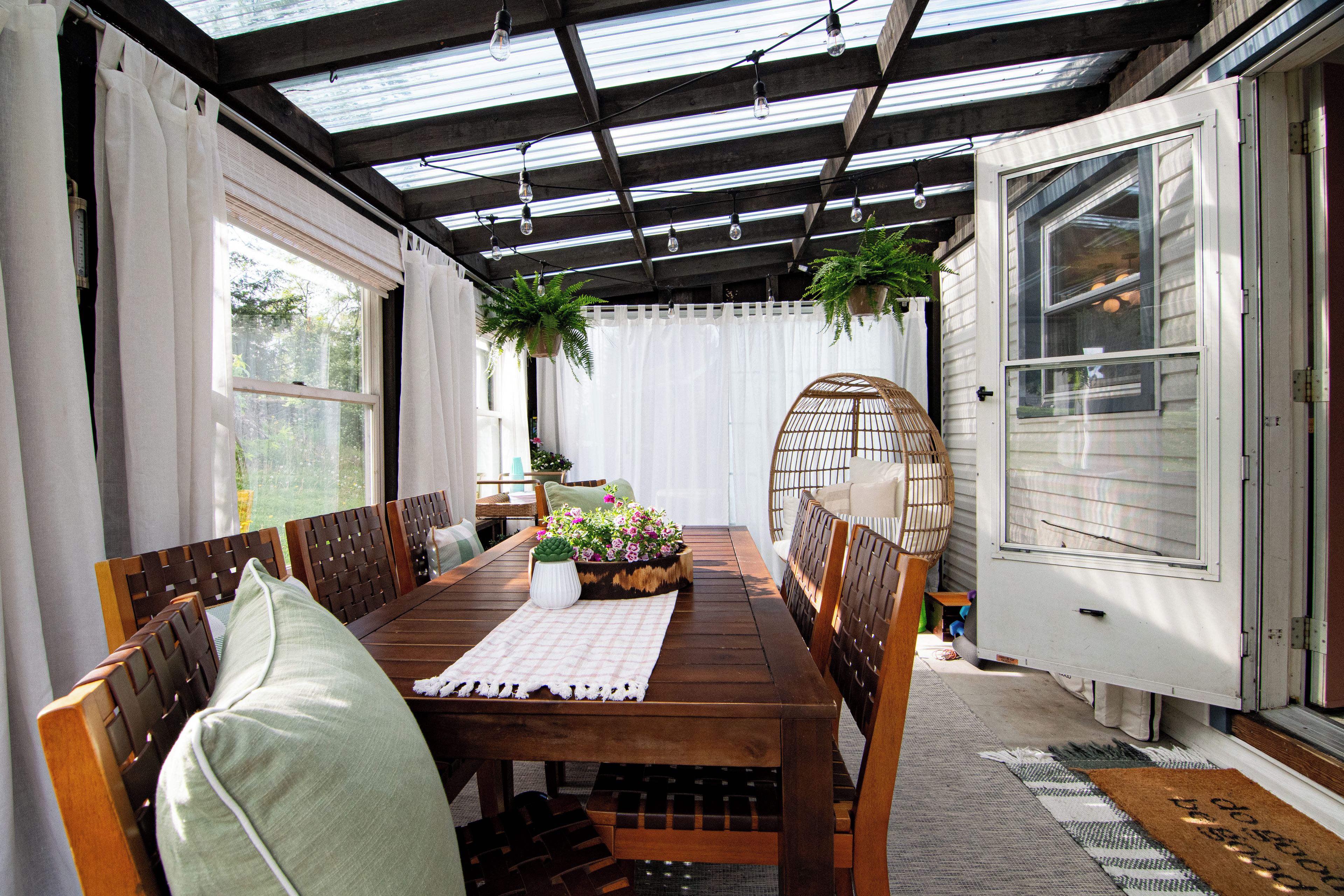 A covered patio with a wooden table, chairs, and hanging plants.