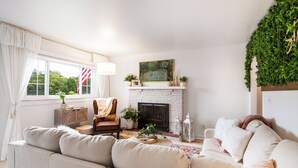 Una sala de estar con chimenea, un sofá, una butaca y un ventanal con cortinas.