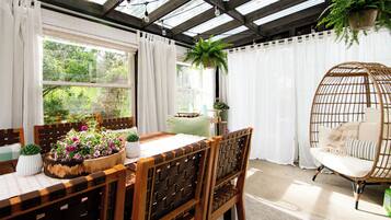 Una habitación con una mesa de madera, sillas, una silla colgante y plantas en macetas.
