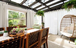 Una habitación con una mesa de madera, sillas, una silla colgante y plantas en macetas.