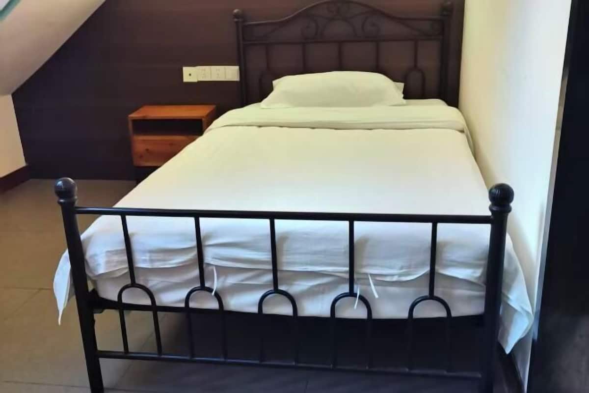 Un lit simple avec un cadre en métal, une table de chevet en bois et une prise électrique murale.