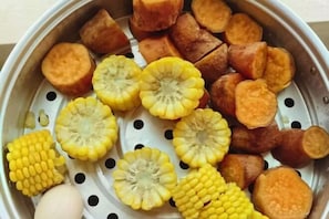 Un panier vapeur contenant des patates douces et du maïs coupés en tranches.