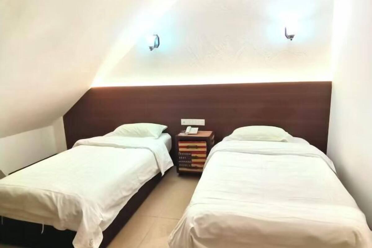Une chambre avec deux lits simples, une tête de lit en bois, une table de chevet avec un téléphone et une pile de livres.