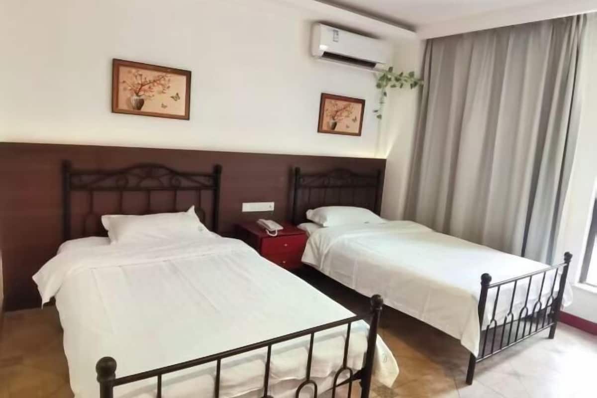 Une chambre d’hôtel avec deux lits simples, une table de chevet rouge, un appareil de climatisation et deux tableaux encadrés au mur.