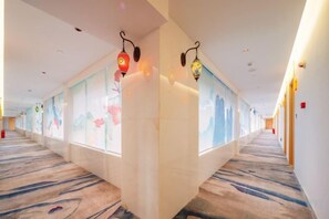 Un couloir d'hôtel doté d'un sol recouvert de moquette, de lampes fixées aux murs et de panneaux de verre décoratifs.