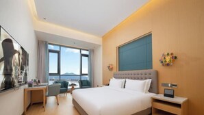 A modern hotel room with a large bed, a desk, a chair, and a view of the sea.