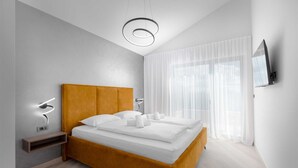 A modern bedroom with a wooden bed, white bedding, a bedside table, a wall-mounted TV, and a large window with sheer curtains. - Villa DIVA I with private pool (Kras)