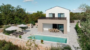 Et moderne hus med to etager, swimmingpool, udendørs møbler og en stenvæg.