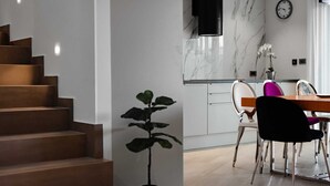 Et moderne køkken med marmor bordplader, et spiseområde med et træbord og stole, samt en trappeopgang med en potteplante.