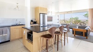 Een moderne keuken met een centraal eiland, barkrukken en een zithoek met een bank en tafel.