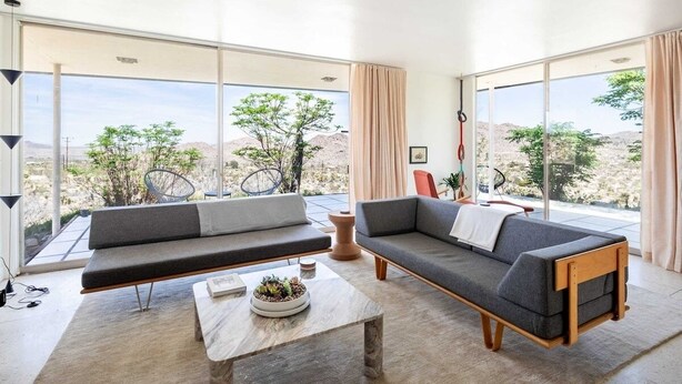 Een moderne woonkamer met twee grijze banken, een salontafel met een plant en grote ramen met uitzicht op een woestijnlandschap.