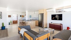 Een moderne woonkamer met een bank, een eettafel en een keuken met een koelkast en kasten.