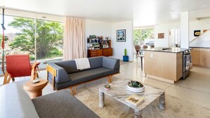 Een moderne woonkamer met een bank, een salontafel en een keukenhoek met een eettafel en aanrecht.