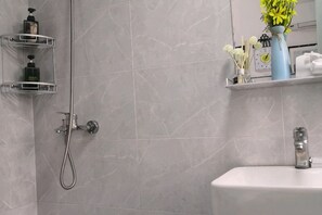 A bathroom with a shower, a sink, and a shelf with toiletries.