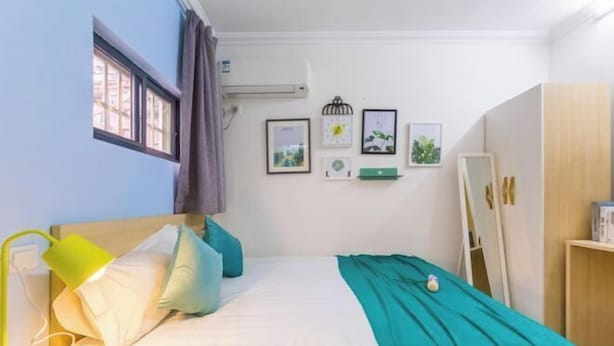 A bedroom with a bed, pillows, a bedside lamp, a window, a wall-mounted air conditioner, and framed pictures. - Ping'an Hotel (Shanghai)