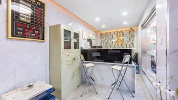 A hotel reception area with a reception desk, chairs, a cabinet, and a wall-mounted display.