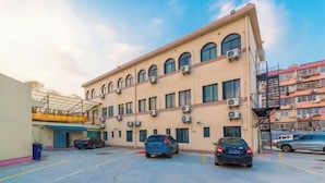 A multi-story building with air conditioning units, a parking lot with several cars, and a staircase leading to an upper level. - Ping'an Hotel (Shanghai)