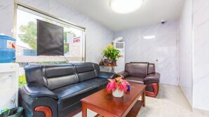 A modern living room with a black leather sofa, a wooden coffee table, and a grey armchair. A large window provides natural light, and an air conditioning unit is mounted on the wall. - Ping'an Hotel (Shanghai)