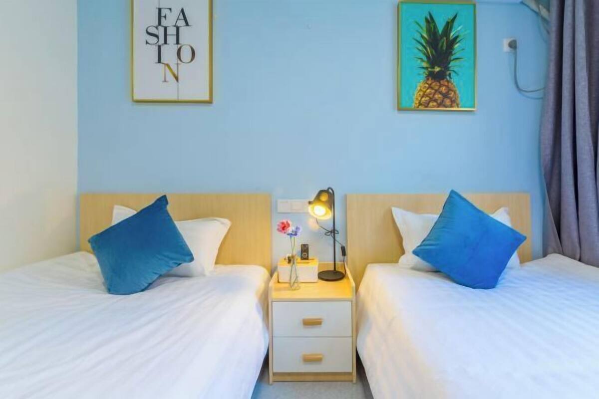 Habitació d'hotel amb dos llits, una taula de nit amb una làmpada, i un quadre de piña a la paret.