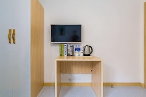 Een kamer met een houten tafel, een flatscreen televisie, boeken, een waterkoker en een klein kastje.