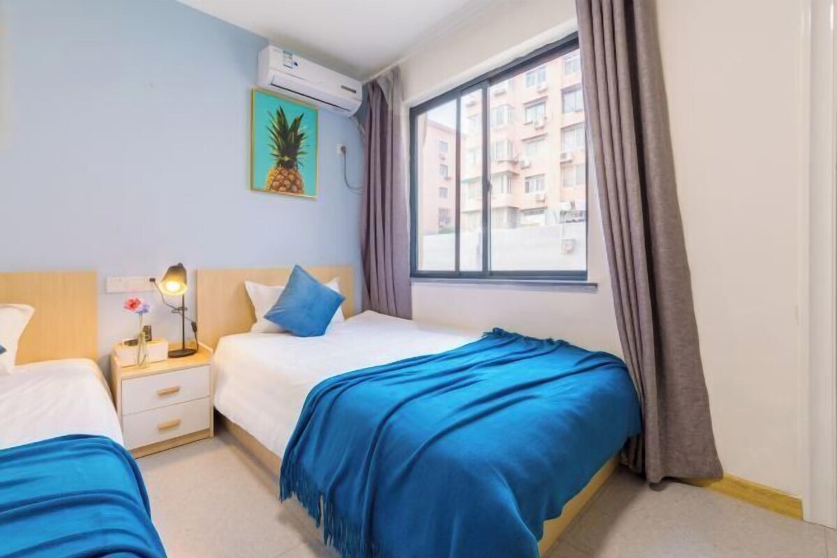 Habitación de hotel con dos camas, una ventana con cortinas, aire acondicionado de pared y un cuadro enmarcado.