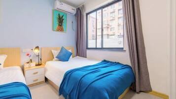 Habitación de hotel con dos camas, una ventana con cortinas, aire acondicionado de pared y un cuadro enmarcado.