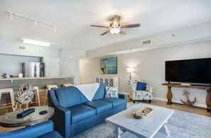 Uma sala de estar moderna com um sofá azul, uma mesa de centro, uma TV e um ventilador de teto.