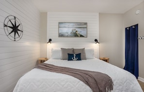 A bedroom with a bed, a compass wall decoration, a painting, and a blue curtain.