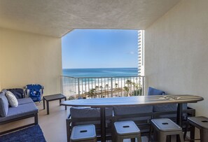 Uma varanda com vista para a praia, um sofá, uma mesinha e um banco de bar.