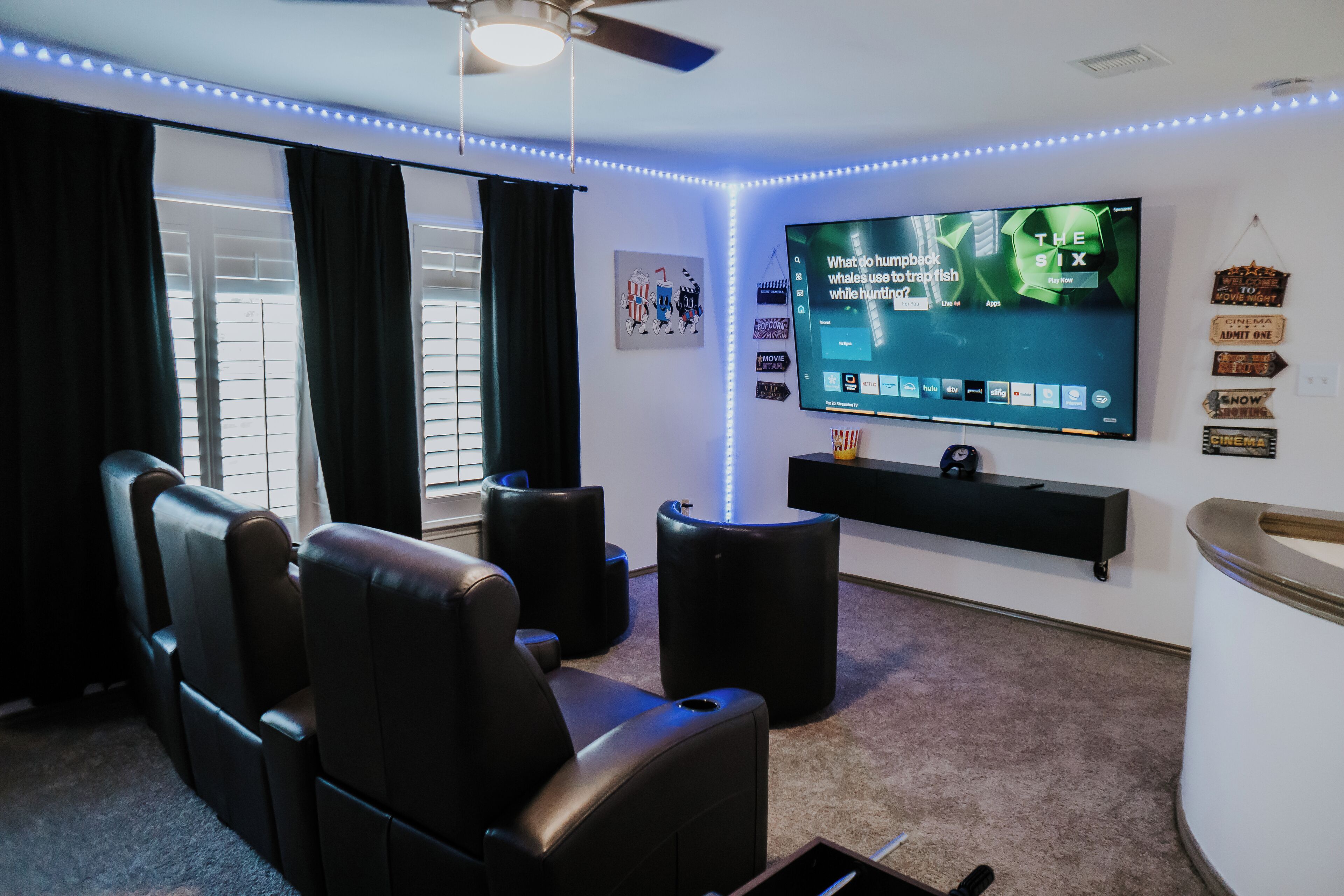 Ein Heimkino mit einem großen Flachbildfernseher, schwarzen Ledersessel und Deckenventilator.