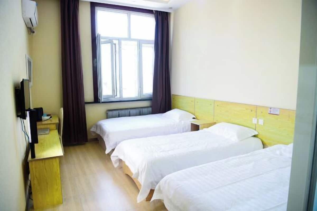 Une chambre d’hôtel avec deux lits simples, un bureau en bois, une fenêtre avec des rideaux et un radiateur.