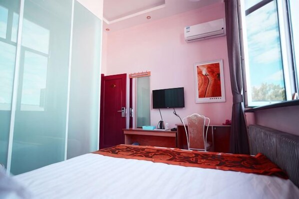 A hotel room with a bed, a desk, a television, and an air conditioning unit. - Jinkelai Hotel (Huma)
