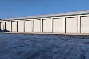Una hilera larga de puertas de garaje metálicas cerradas, suelo pavimentado y cielo despejado.