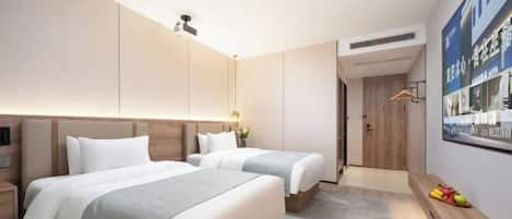 A hotel room with two beds, a wooden headboard, a wall-mounted TV, and a small shelf with fruit.
