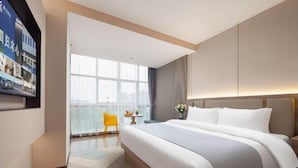 A modern hotel room with a large bed, a small table with a vase of flowers, and a view of the city through large windows. - Skyscraper Hotel (Wenling Jingyuan Branch) (Wenling)