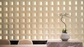 A reception area with a marble table, chairs, and a potted plant against a patterned wall.