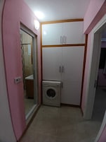Una habitación compacta con lavadora, armario y espejo.